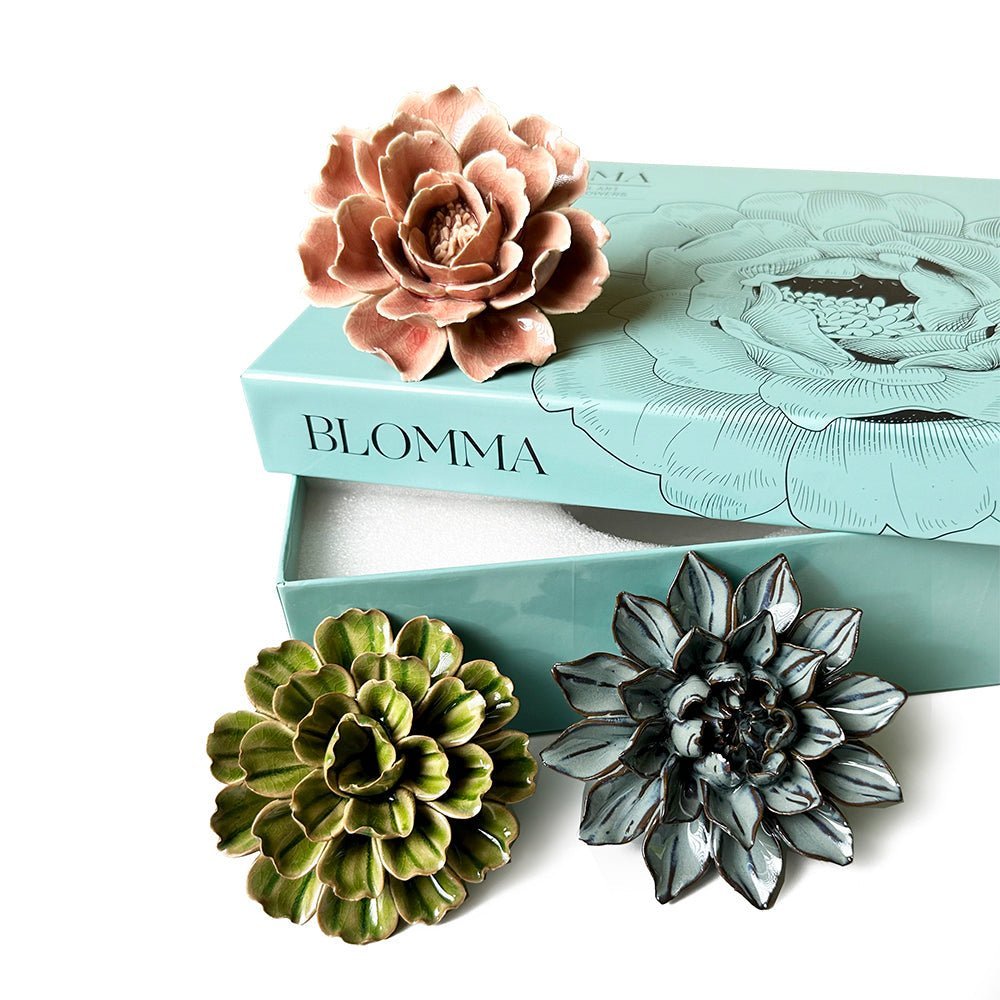 Three flower-shaped ceramic wall decor pieces in pink, green, and blue are displayed with an elegant teal box labeled "Blomma," featuring a flower illustration.