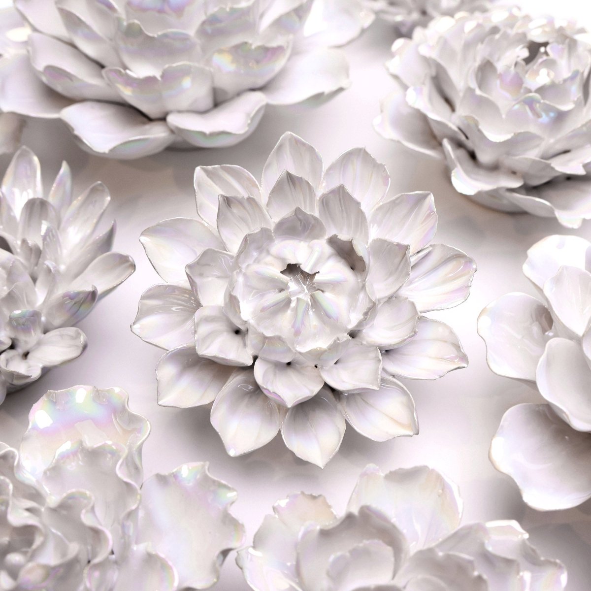 Close-up of several white ceramic flowers arranged closely together. The flowers have delicate, layered petals with a slightly glossy finish, creating an elegant and intricate pattern against a light background.