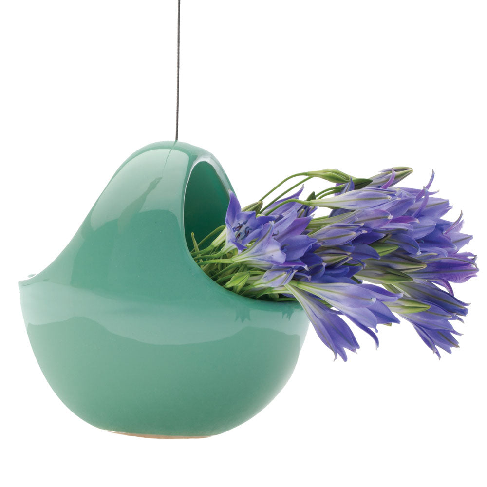 A green Chive Studio 2024 hanging aerium ceramic for succulents & ikebana shaped like a bird, filled with vibrant purple flowers, isolated on a white background.