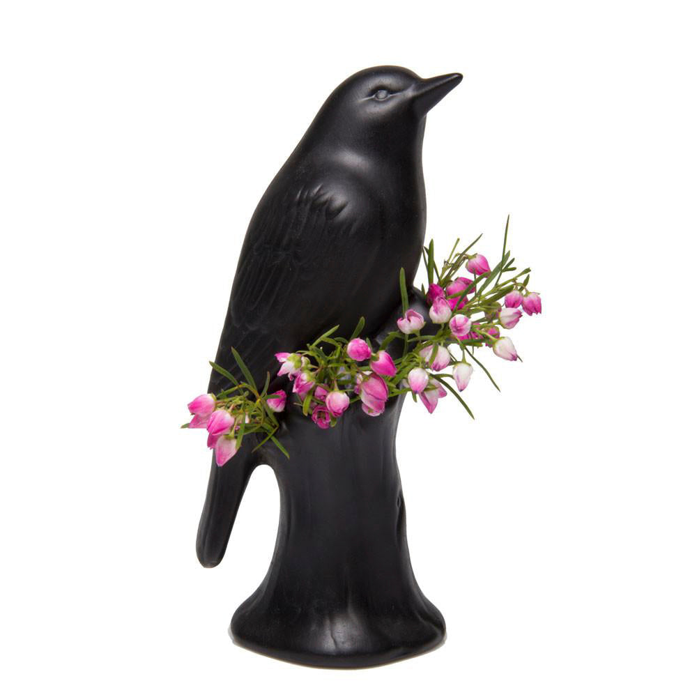 A black ceramic Bird Porcelain Modern Flower Vase figurine with a small bouquet of pink flowers tucked into its back, representing a Scout merit badge, standing upright on a white background. Brand: Chive Studio 2024