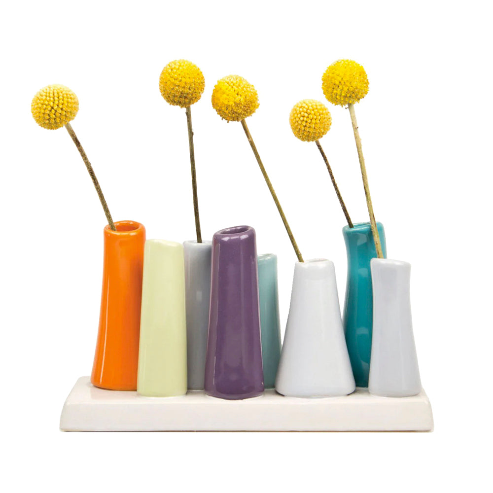 Eight colorful tubes Chive Studio  Pooley Modern Bud Vases for flowers attached to a white base, each holding a round, yellow flower. The vases are orange, lime green, lavender, cream, white, mint, frost and teal.