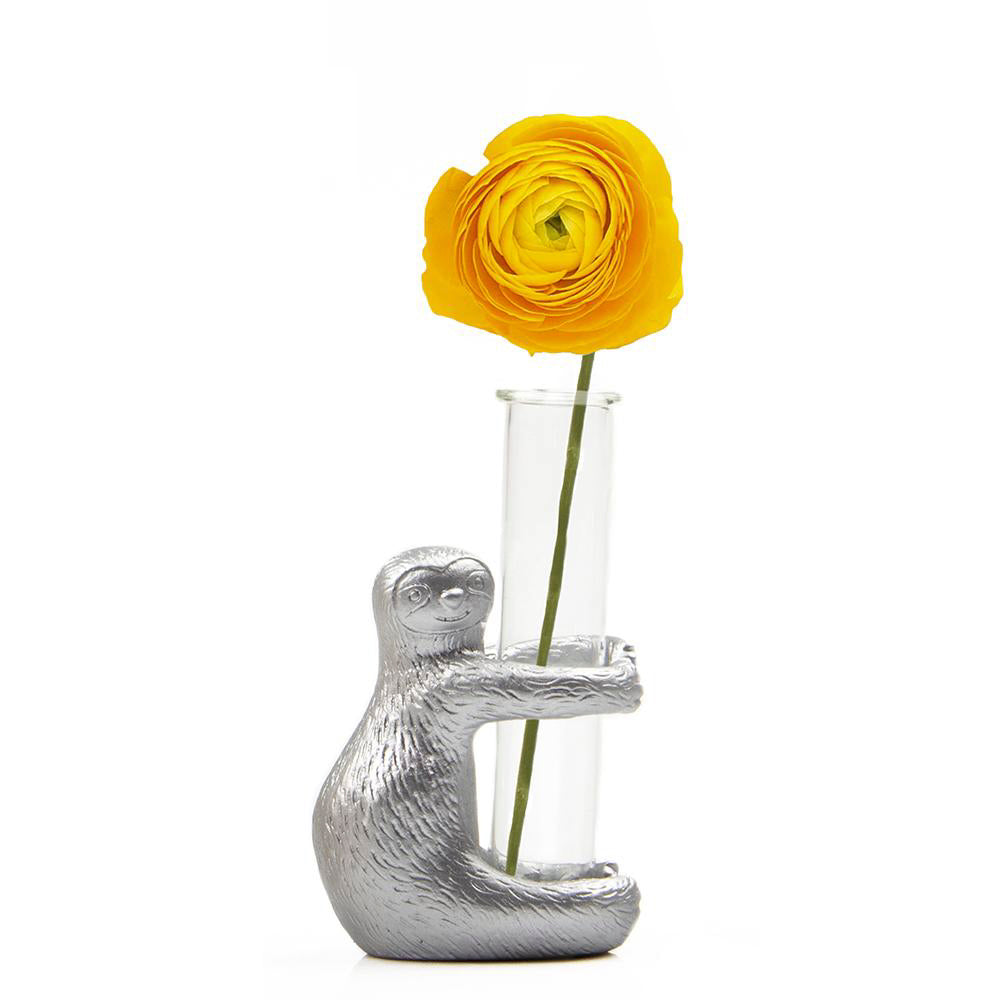 A Sloth Metal & Glass Propagator clutching a clear glass tube vase, containing a single vivid yellow ranunculus flower, set against a plain white background.