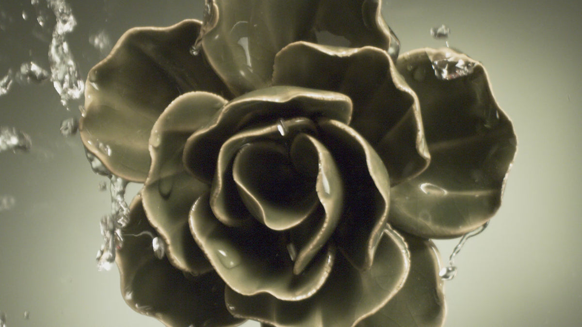Water beads off a hand-glazed green ceramic ranunculus — green wall art that never needs watering.